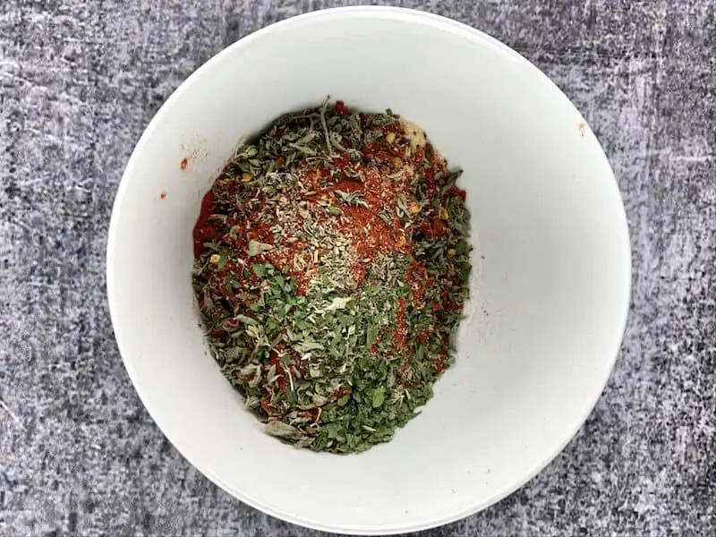 Italian herb seasoning ingredients in a white bowl.