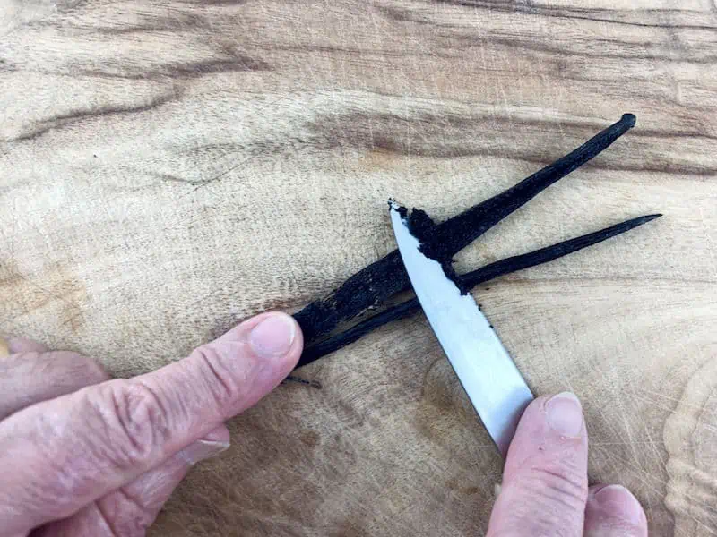 HANDS SCRAPING A VANILLA BEAN POD WITH A KNIFE