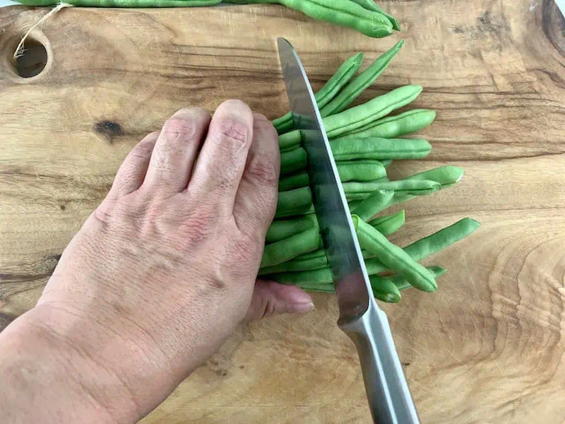 HANDS SLICING GREEN BEANS IN HALF ON WOODEN BOARD