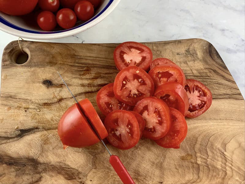 SLICING ROMAS INTO ROUNDS WITH A KNIFE ON A WOODEN CHOPPING BOARD