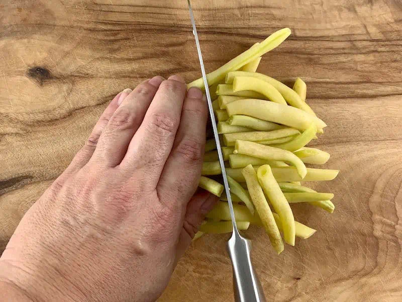 HANDS SLICING YELLOW BEANS IN HALF ON WOODEN BOARD