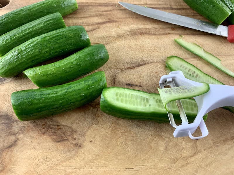 SLICING CUKES INTO RIBBONS WITH Y PEELER ON A WOODEN BOARD