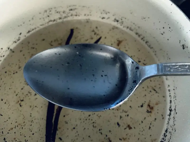 SPOON WITH VANILLA BEAN SYRUP OVER PAN SHOWING DISSOLVED SUGAR