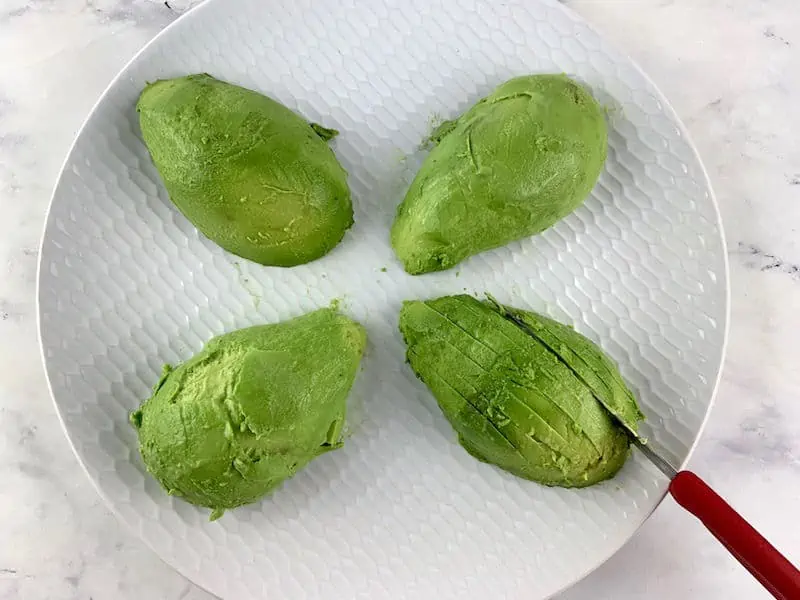 SLICING AVOCADO ON A WHITE PLATE WITH A RED KNIFE