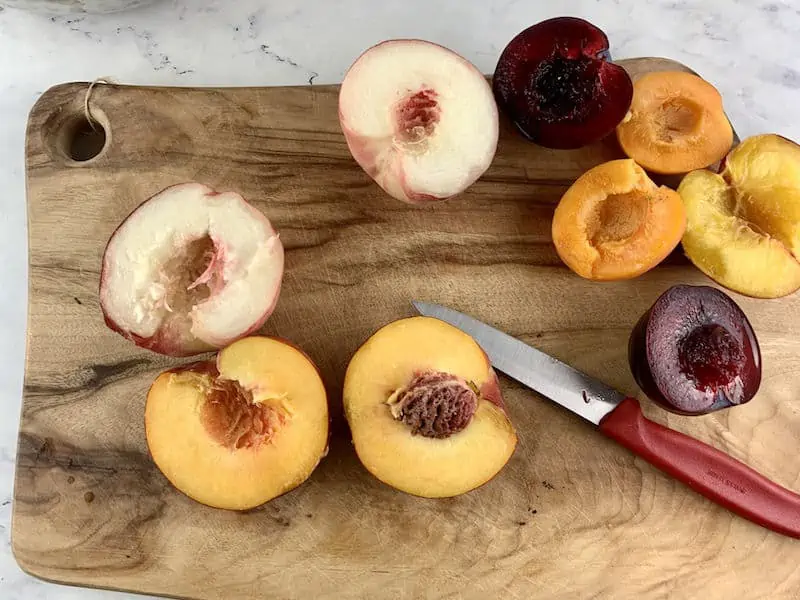 HALVED STONE FRUIT ON WOODEN BOARD WITH RED KNIFE
