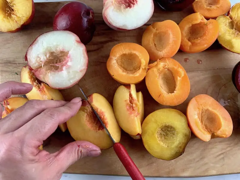 HANDS SLICING STONE FRUIT WITH A RED KNIFE ON A WOODEN BAORD