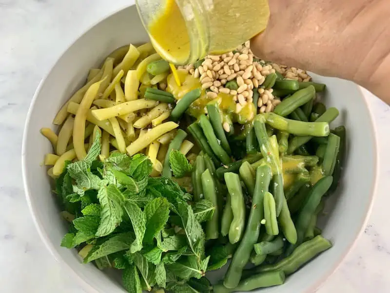 POURING OVER MUSTARD DRESSING ON YELLOW BEAN SALAD INGREDIENTS