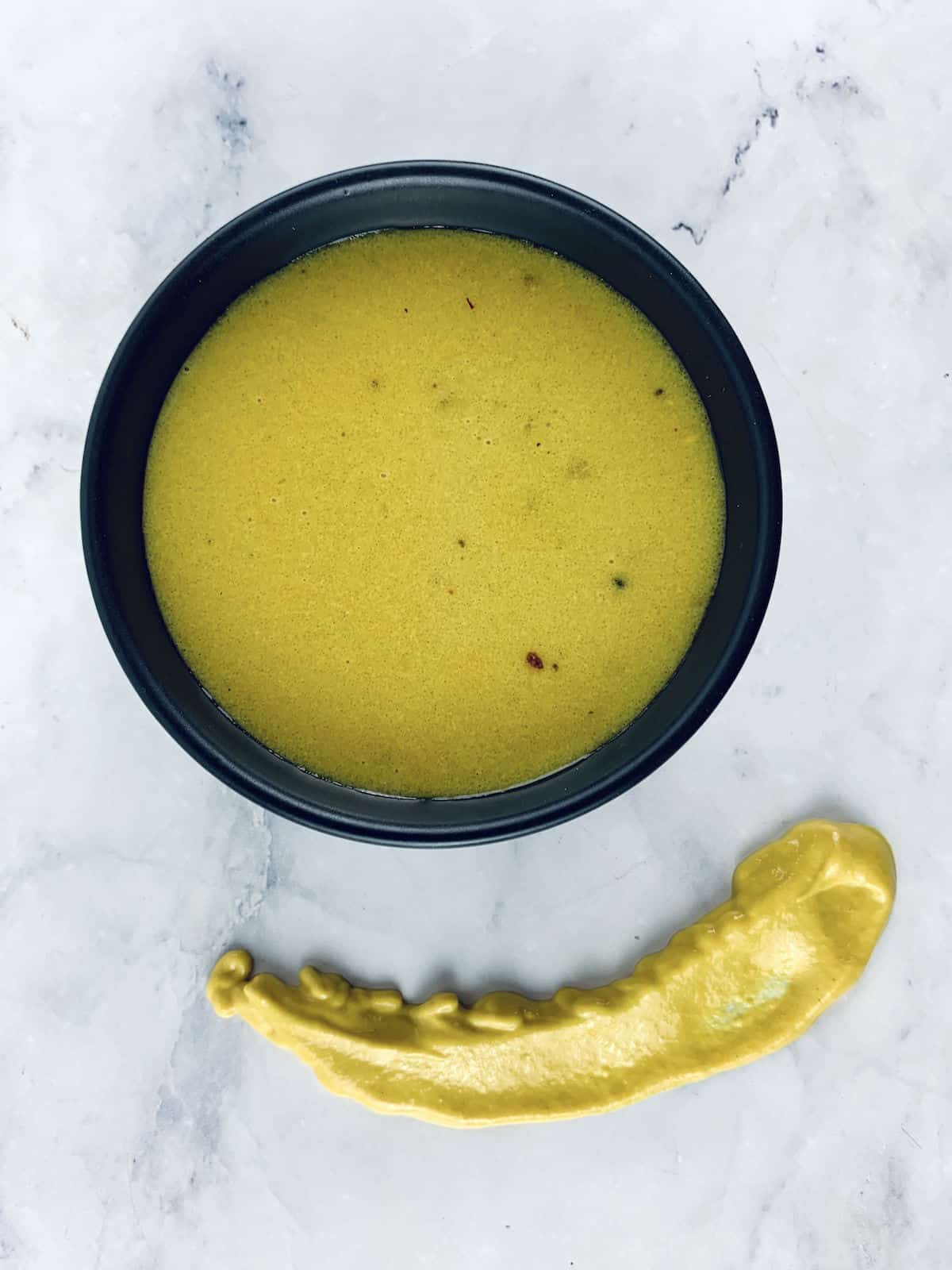 AMERICAN MUSTARD DRESSING IN A BLACK BOWL WITH A YELLOW MUSTARD SMEAR ON THE SIDE