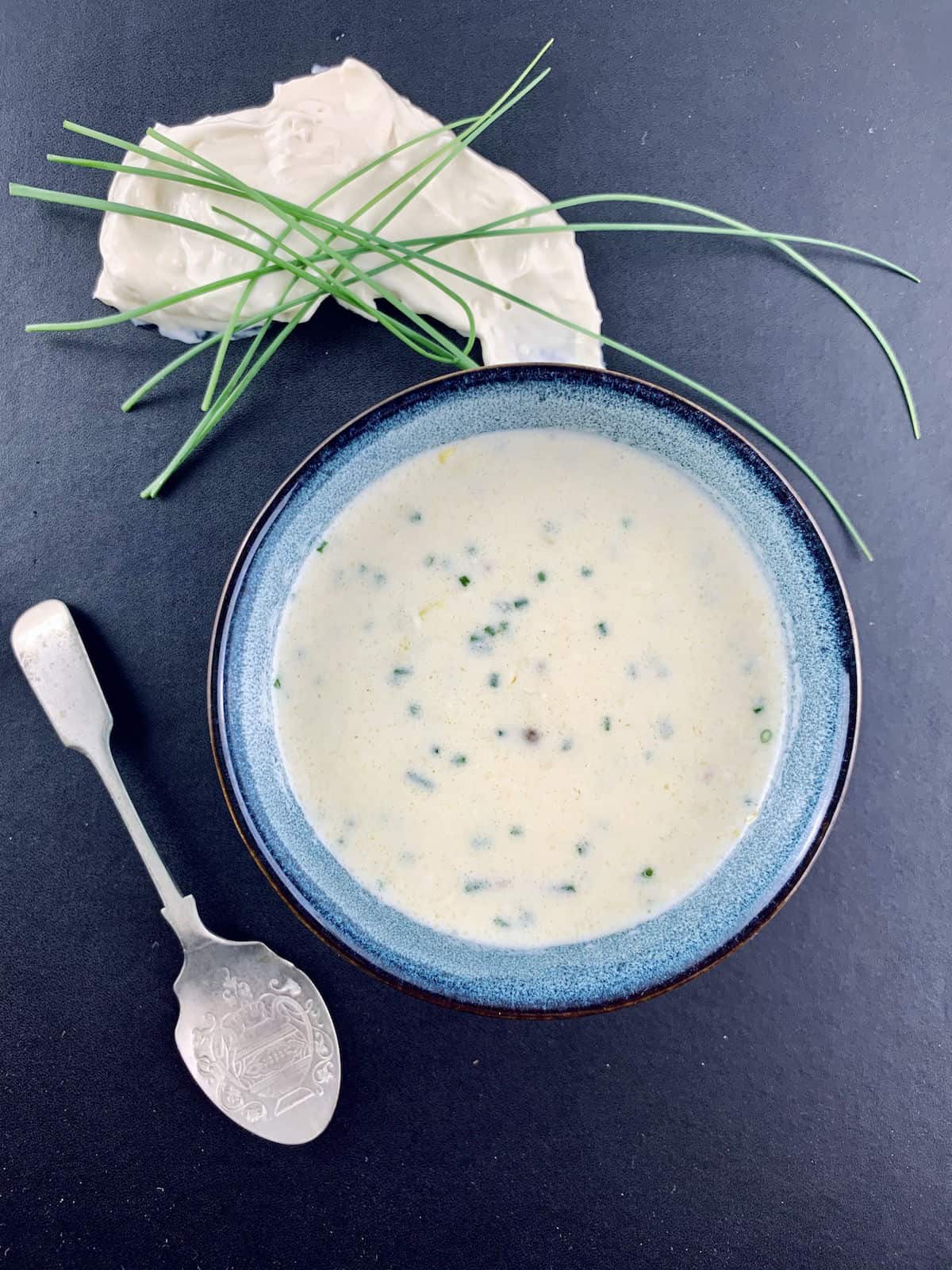 Buttermilk dressing in blue bowl with silver spoon, cream cheese and chives on the sidde