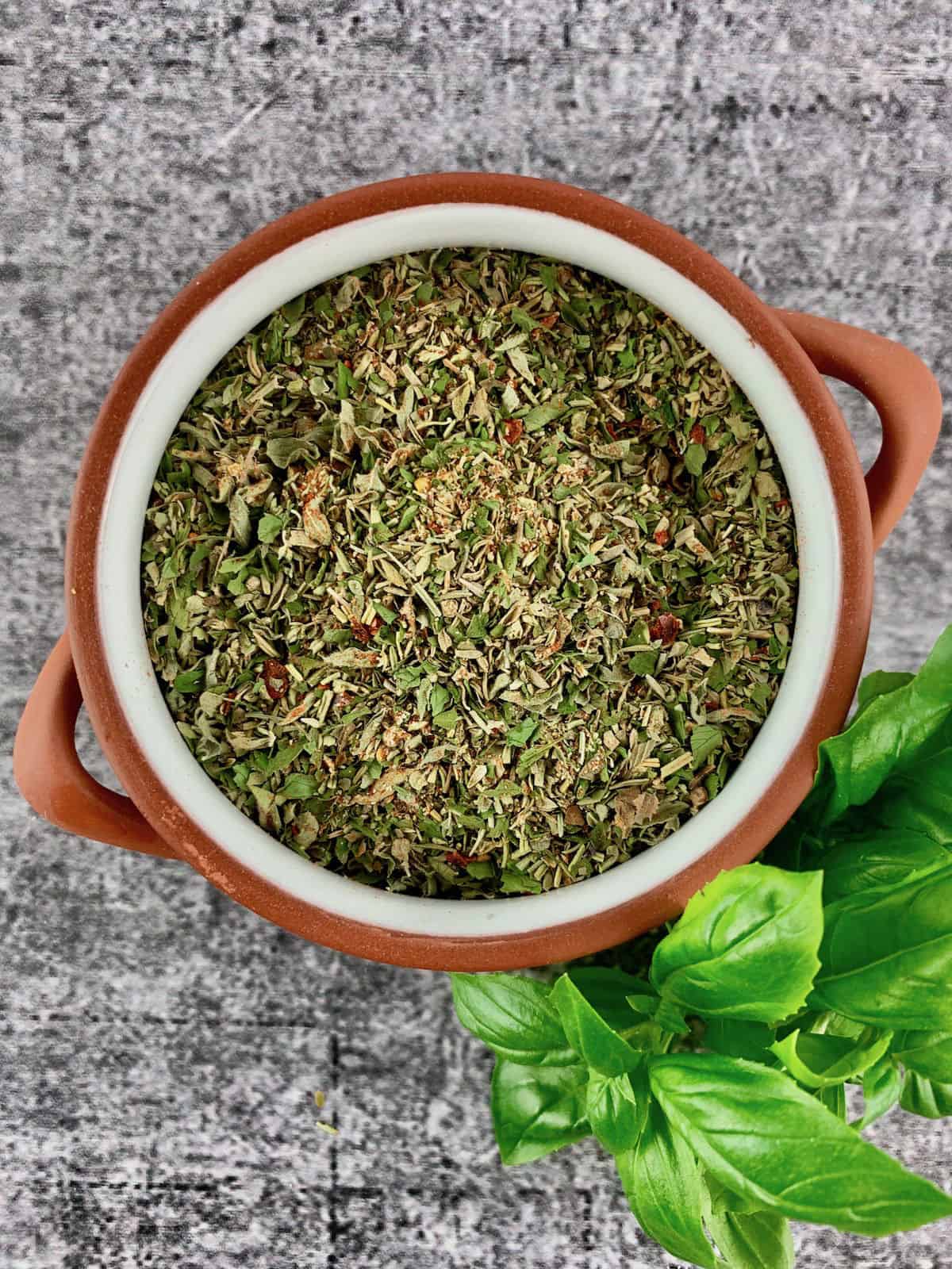 ITALIAN HERB SEASONING IN TERRACOTTA BOWL WITH BASIL SPRIG ON THE SIDE