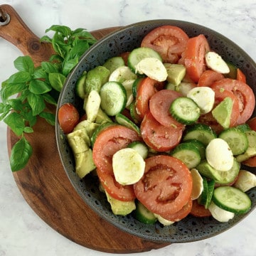TRICOLORE SALAD IN A DARK GREY BOWL SITTING ON WOODEN BOARD WITH BASIL SPRIGS ON THE SIDE