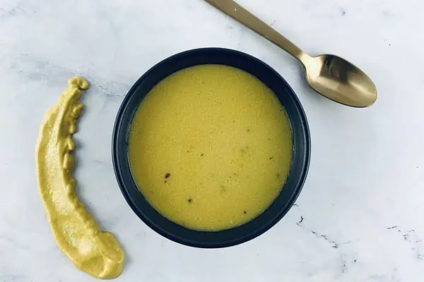 American mustard dressing in a black bowl with a yellow mustard smear on the side & a gold spoon
