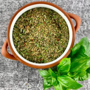 Italian herb seasoning substitute in terracotta bowl with basil sprig on the side.