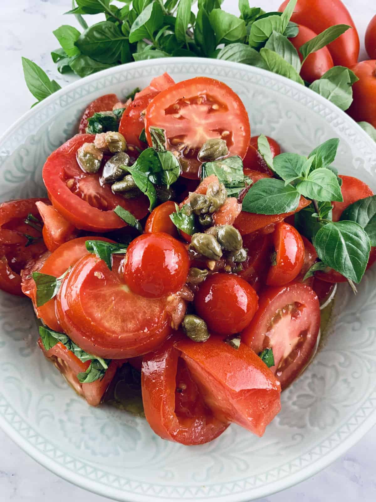 Italian tomato salad in a mint bowl with tomatoes and basil on the side.