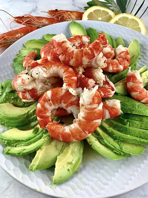 SHRIMP AND AVOCADO SALAD ON A WHITE PLATE WITH PRAWNS AND LEMON SLICES ON THE SIDE