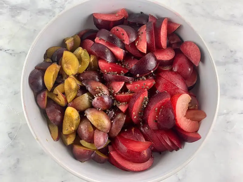 CUT PLUMS & CARDAMOM SEEDS IN A WHITE BOWL