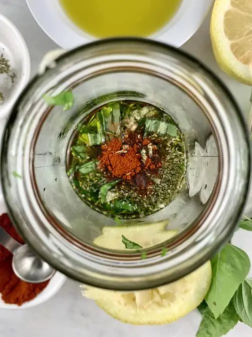 Italian vinaigrette ingredients in a blender with basil and herbs in background.