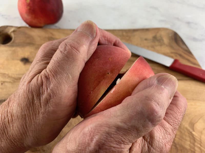 HANDS TWISTING PEACH HALVES ON A WOODEN BOARD
