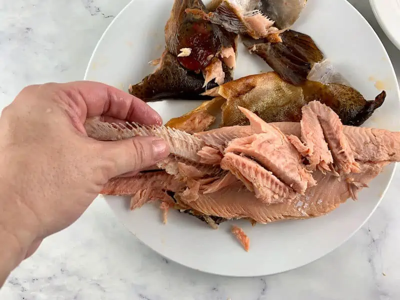 HANDS REMOVING BONES FROM SMOKED TROUT ON WHITE PLATE