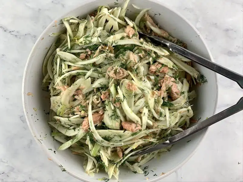 TOSSING SMOKED TROUT & FENNEL SALAD WITH TONGS IN WHITE BOWL