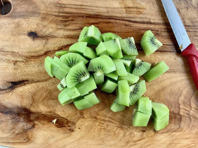 DICED UP KIWI FRUIT ON WOODEN BOARD WITH RED KNIFE