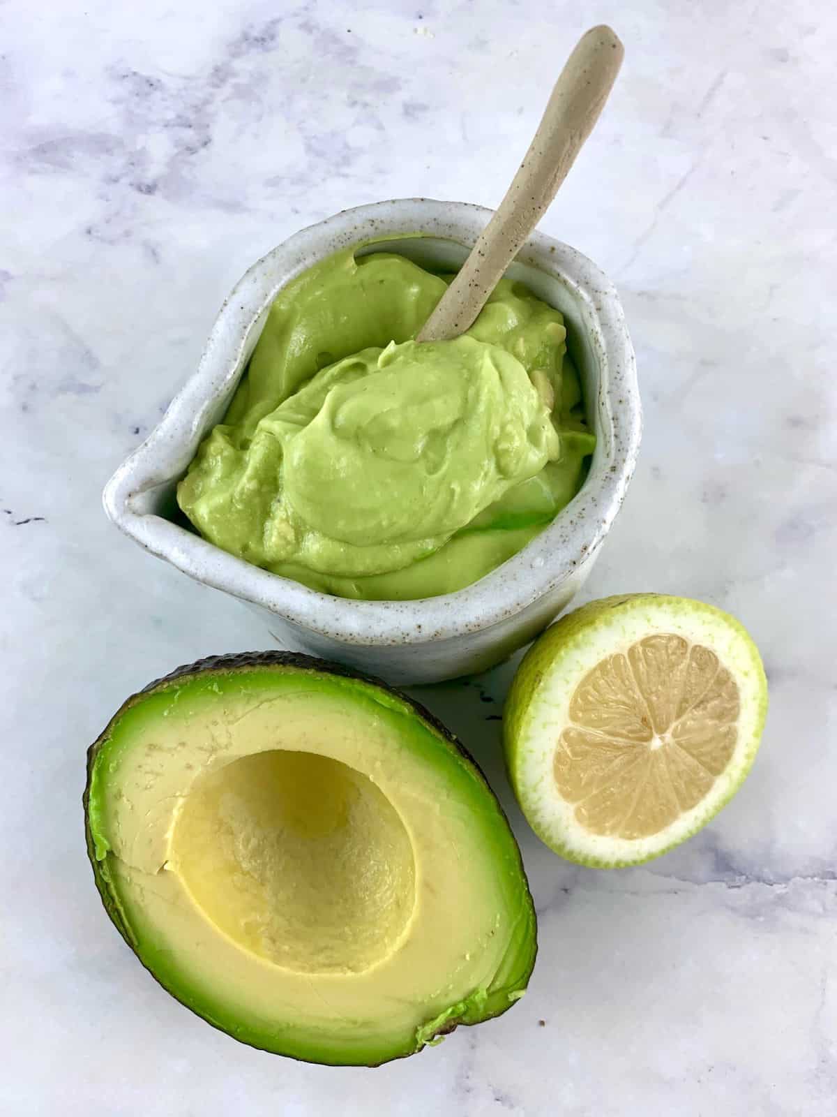 avocado mayo in a white pottery jug with avocado half, lemon half and spoon on the side