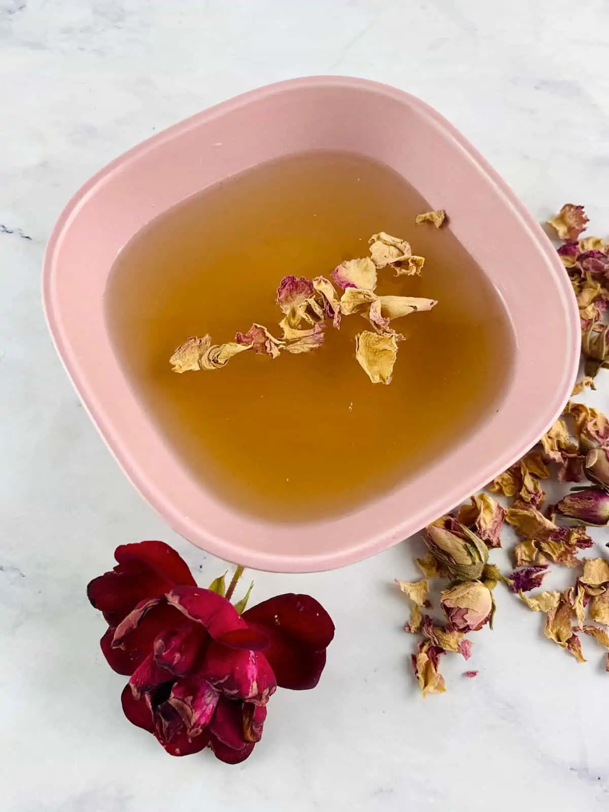 CARDAMOM SYRUP IN A PINK BOWL WITH ROSE & ROSE PETALS ON THE SIDE