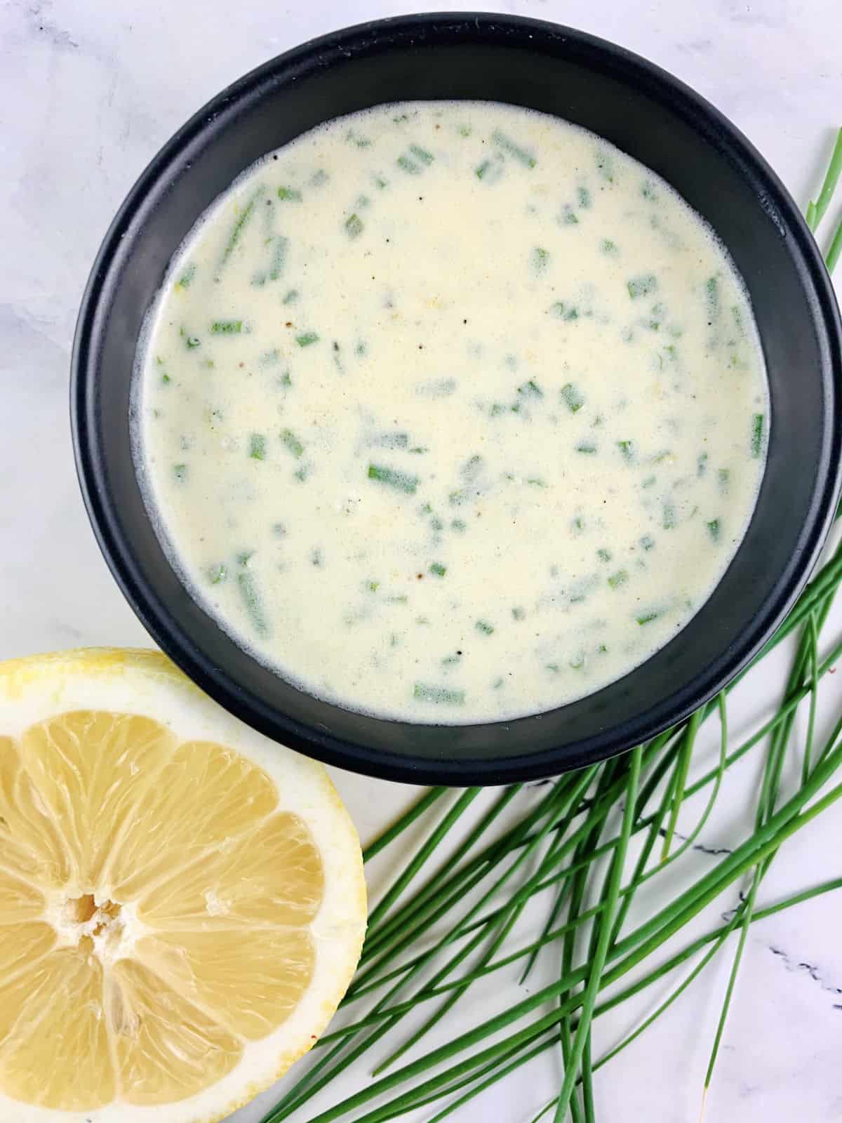 SOUR CREAM & CHIVE DRESSING IN A BLACK BOWL WITH CHIVES AND LEMON ON THE SIDE