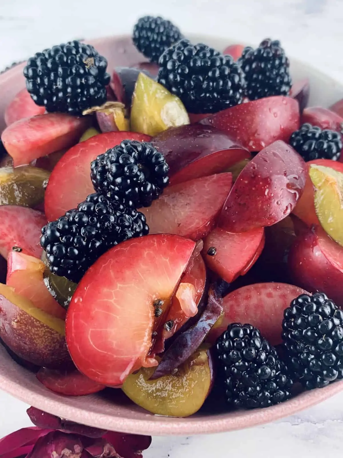 Plum Salad with Blackberries in a pink bowl with a rose bottom left corner.