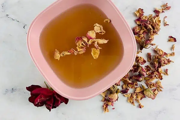 Cardamom syrup in a pink bowl with rose and rose petals on the side.