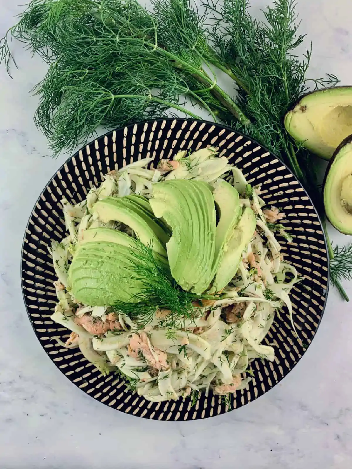 Smoked trout & fennel salad on a patterned platter with dill & avocado on the side.