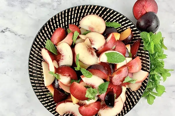 White peach salad on a black patterned plate with plums and mint on the side.