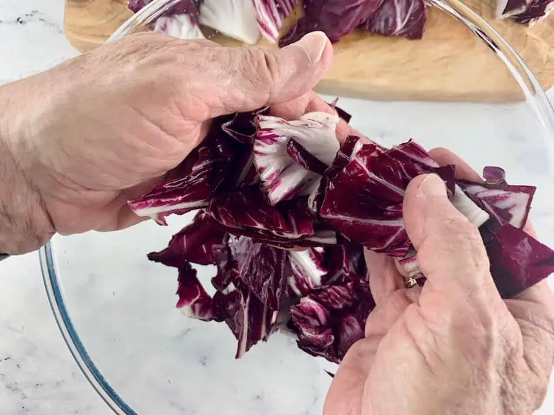 HANDS SEPARATING RADICCHIO LEAVES OVER A GLASS BOWL