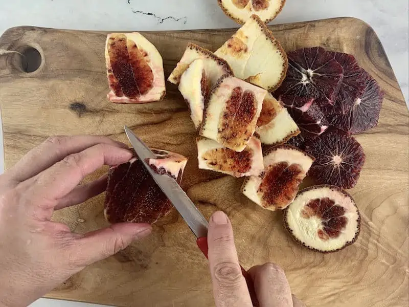 HANDS TRIMMING PITH FROM BLOOD ORANGE ON WOODEN BOARD
