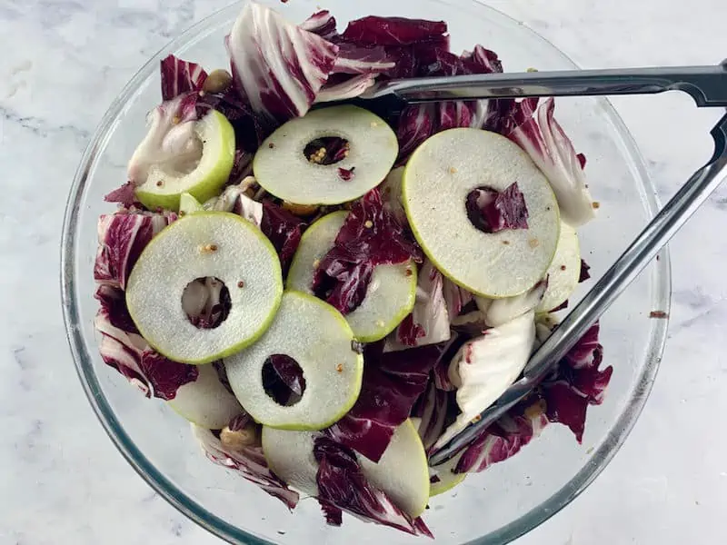 MIXING RADICCHIO SALAD IN A GLASS BOWL WITH TONGS