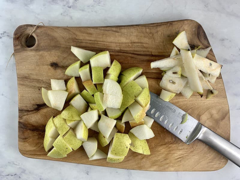DICED UP PEAR ON WOODEN BOARD WITH KNIFE AND CORE PEARS ON THE SIDE