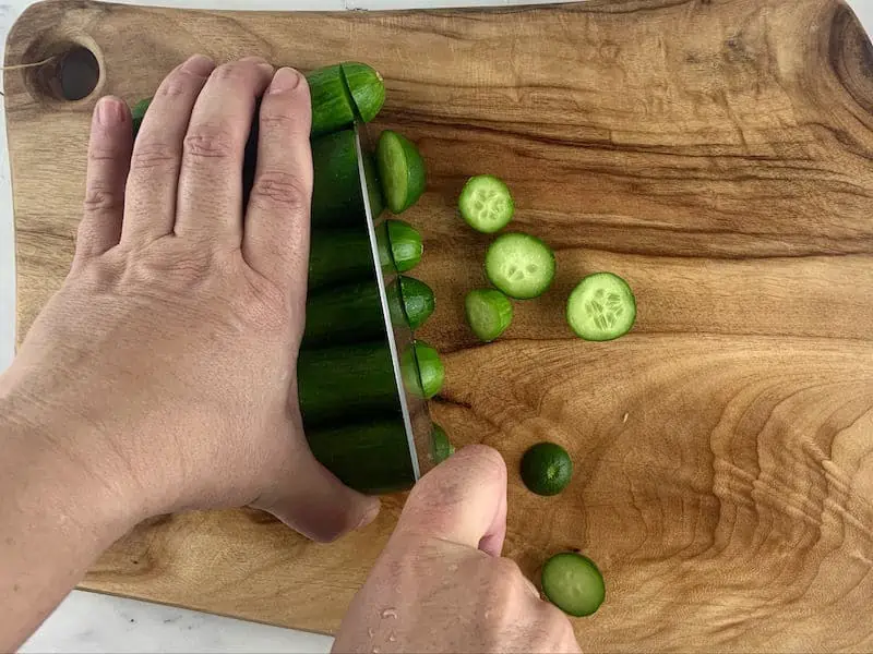 HANDS TRIMMING CUKES ON WOODEN BOARD WITH A KNIFE