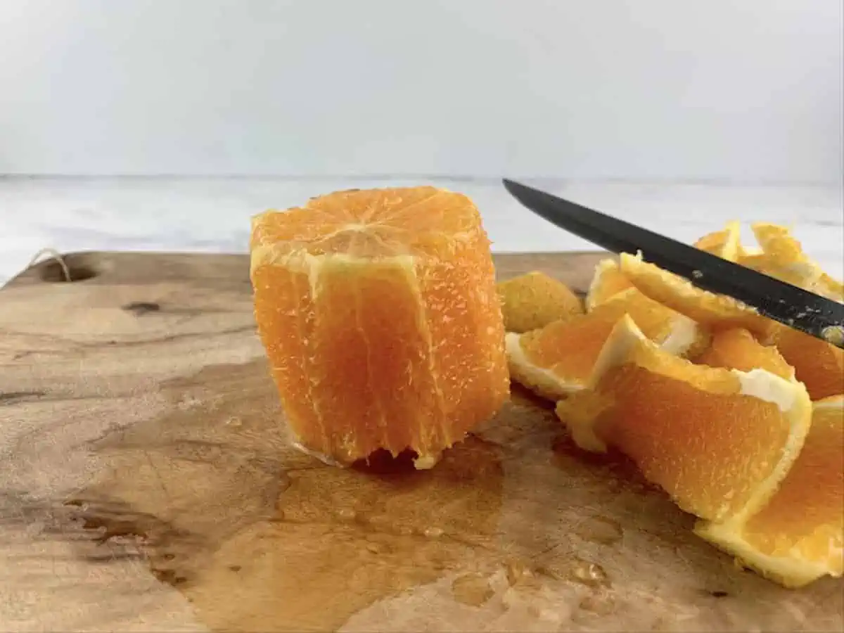 A stood up peeled orange on a wooden board with peel and knife.