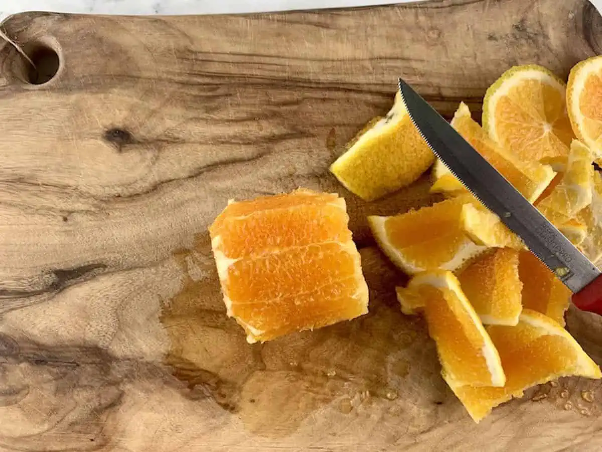 Peeled orange on wooden board with knife and peel.