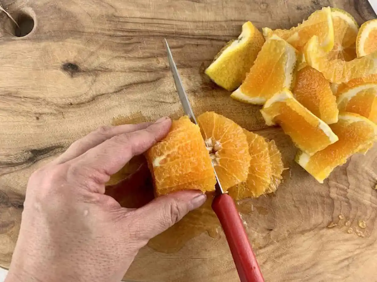 AERIAL VIEW OF HANDS SLICING PEELED ORANGE WITH A RED KNIFE ON WOODEN BOARD