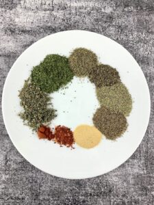 A MIX OF DRIED HERBS AND SPICES ON A WHITE PLATE WITH A GREY BACKGROUND
