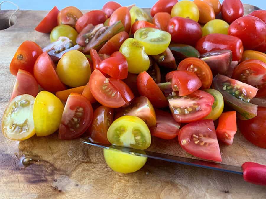 A close-up of a cherry tomato medley with a knife on a wooden board.
