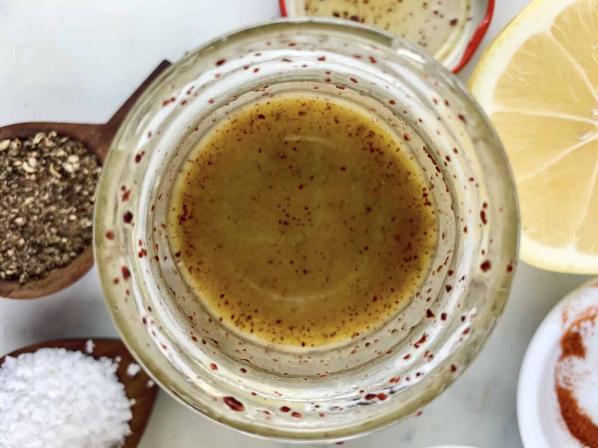 Shaken sumac dressing in a glass jar with ingredients scattered around.