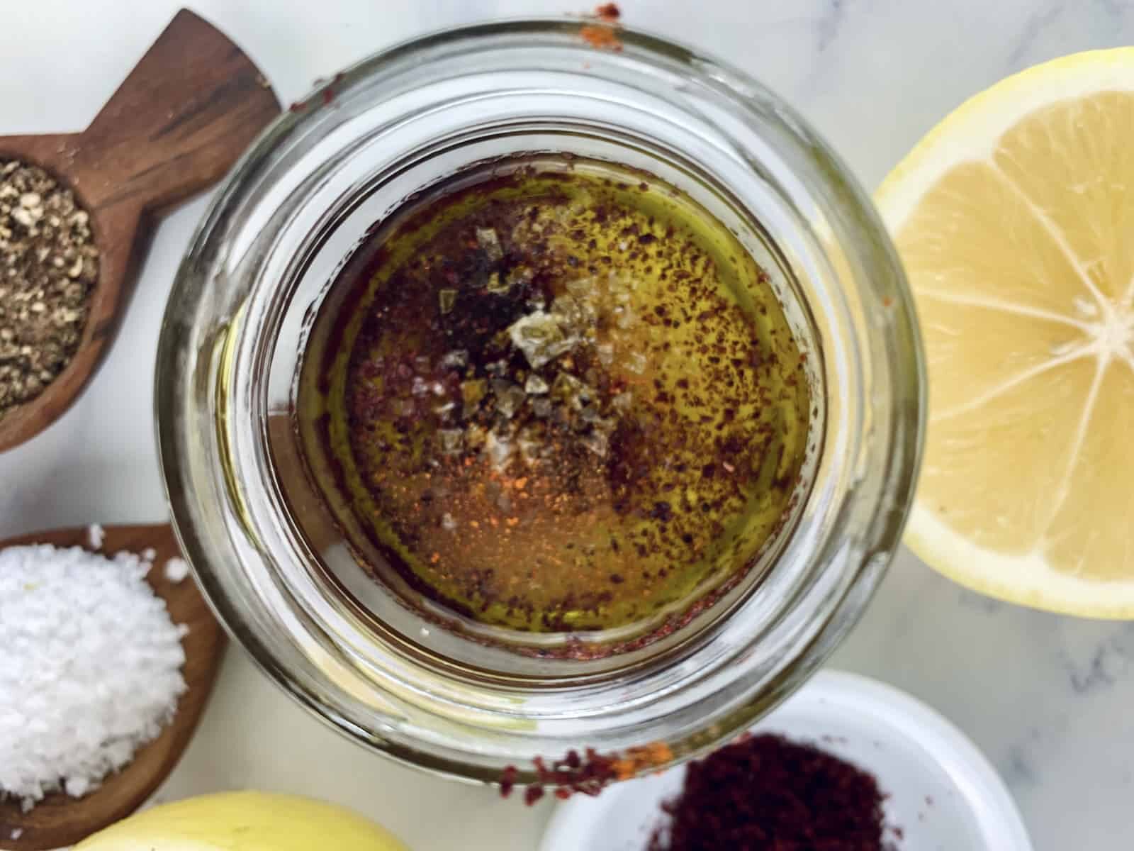 Sumac vinaigrette ingredients in a glass jar with ingredients scattered around.