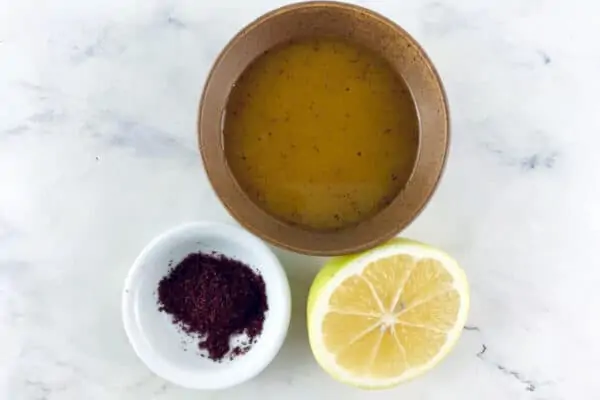 Sumac vinaigrette in a small tan bowl with sumac powder and half a cut lemon in front.