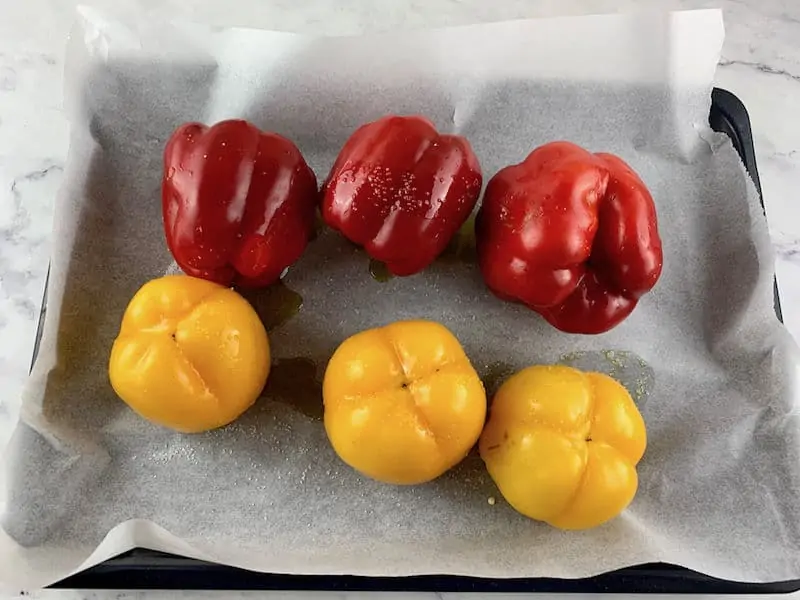 Red and yellow bellow peppers on a baking tray with oil and salt.