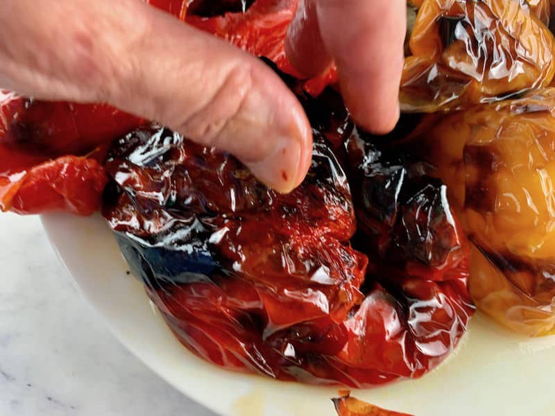 Fingers pinching skin of roasted peppers.