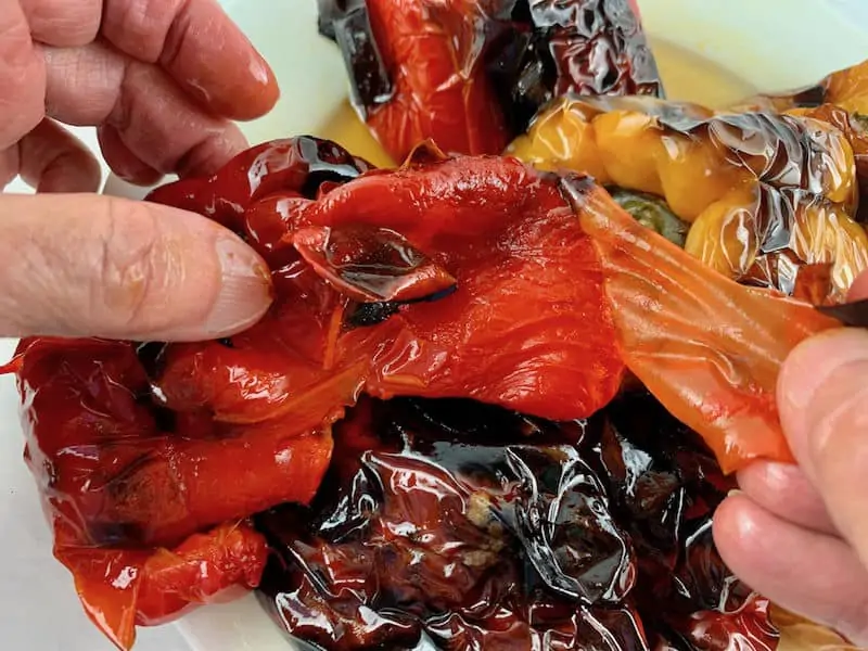 Hands peeling the skin from roasted peppers.