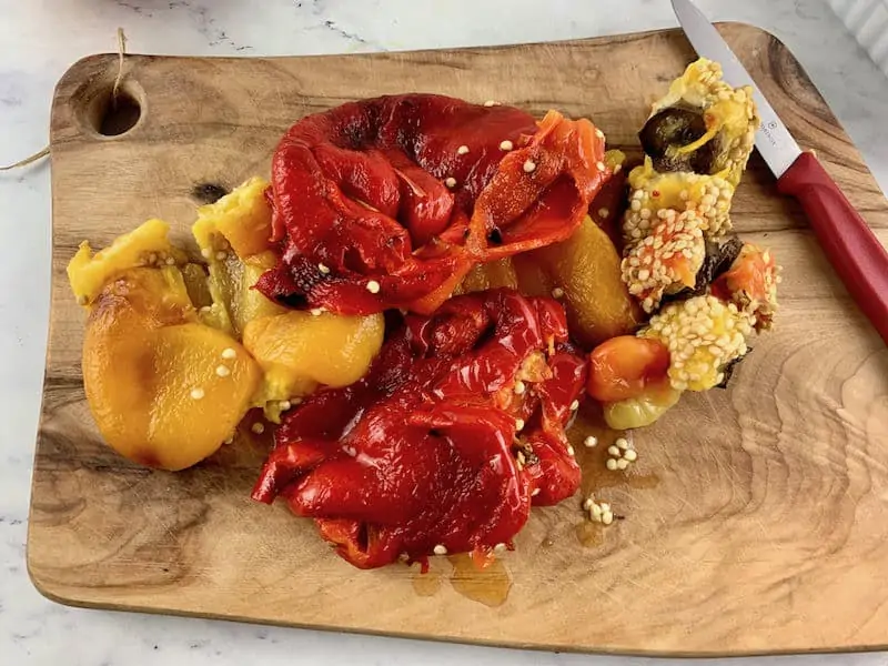 Roasted peppers on a wooden board with a knife on the right, seeds removed.