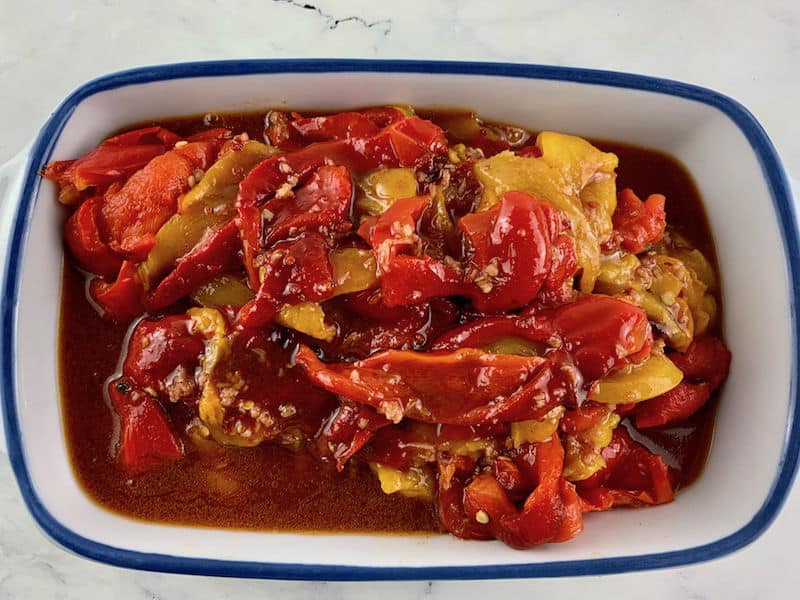Poured dressing over roasted peppers in a ceramic dish with a blue trim.